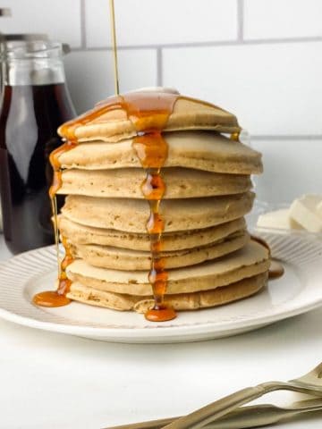Dairy-free pancakes on a white plate with maple syrup pouring over them.