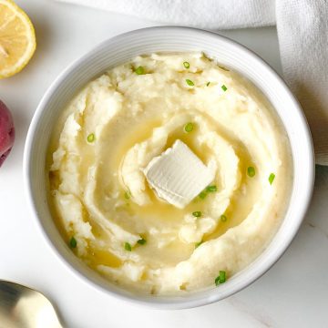 Dairy-free mashed potatoes in a white bowl topped with green onions and melted vegan butter.