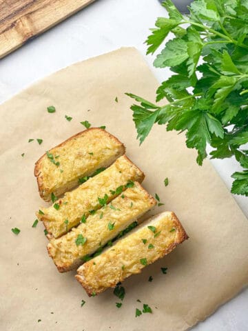 Healthier garlic bread on brown parchment paper, sliced and topped with fresh parsley.