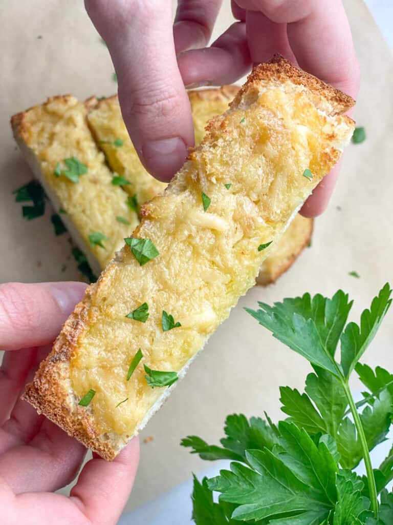 Holding a slice of the garlic bread.