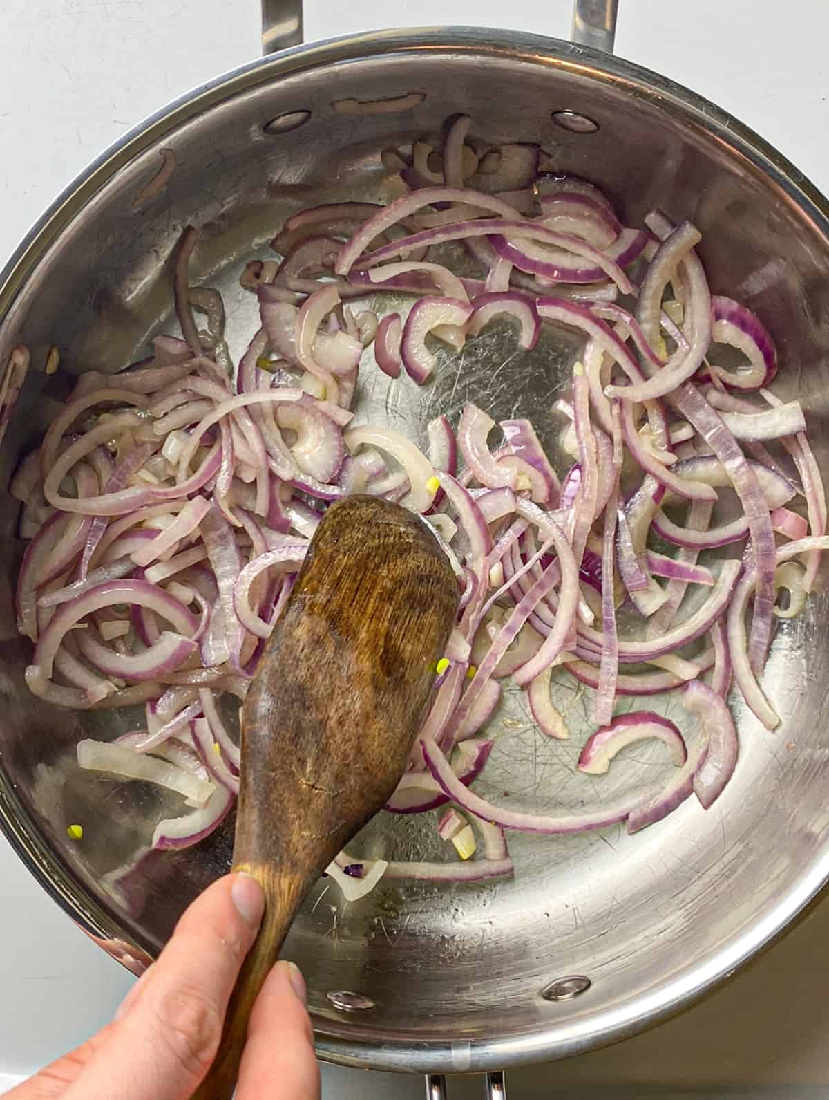 Red onions sautéing in a pan with olive oil. Stirring with a wooden spoon.
