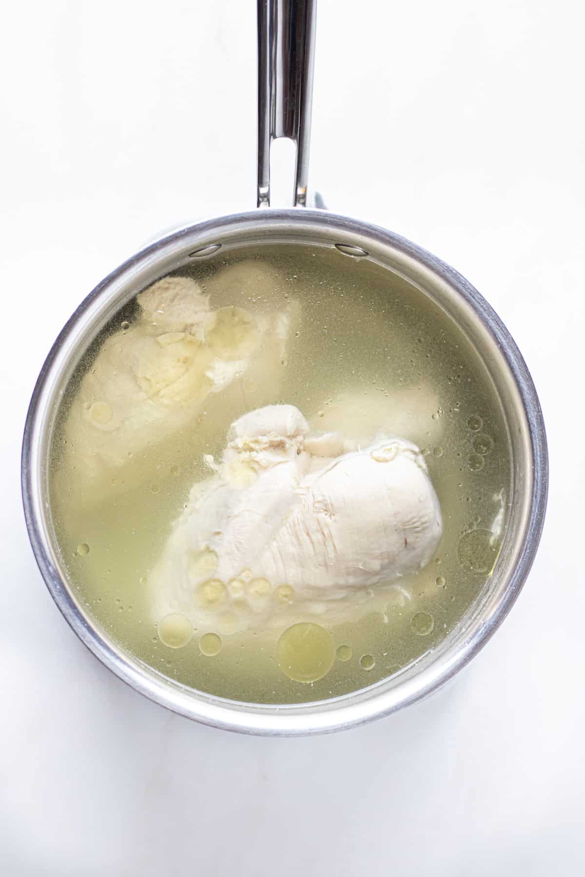 Boiled chicken breasts in a stainless steel pot, submerged in the water.