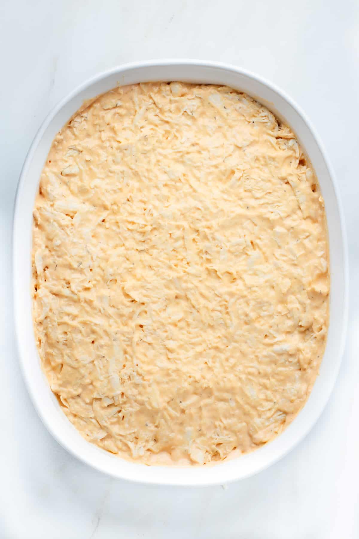 Dairy-free buffalo chicken dip in a shallow white casserole pan before going into the oven.