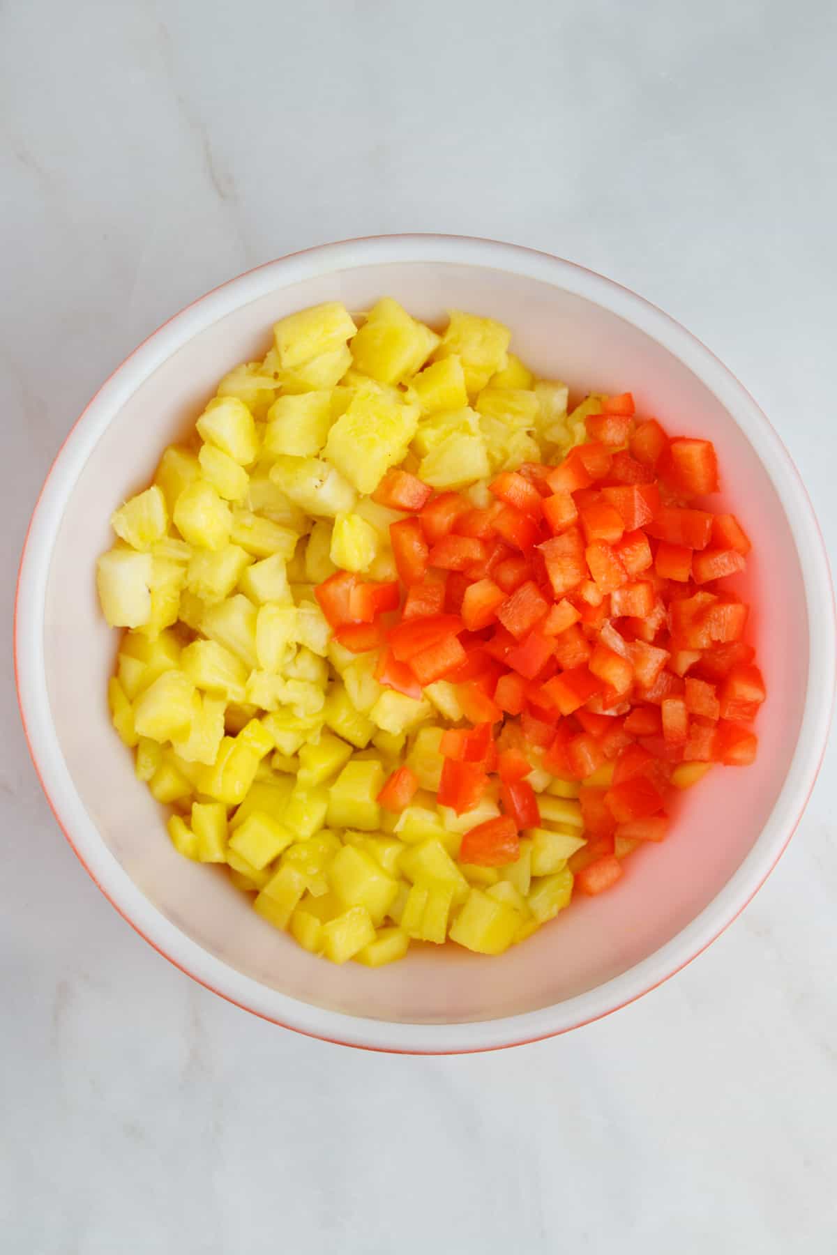 Fresh mangos, pineapples and diced red bell pepper in a bowl.