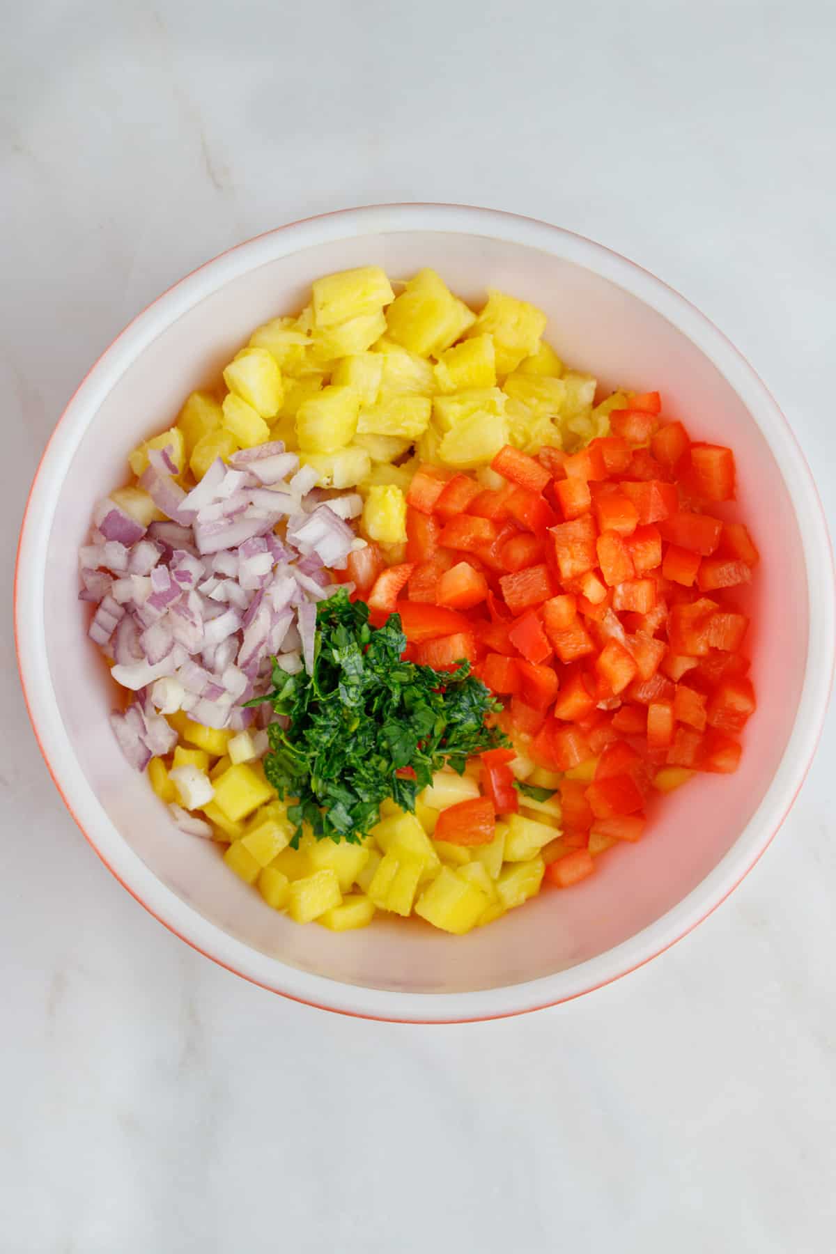 Diced mangos, pineapples, red bell pepper, red onions and cilantro in a bowl.