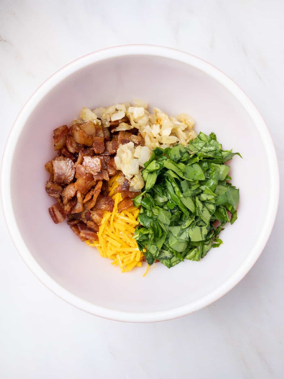 Crispy chopped bacon, dairy-free cheddar cheese shreds, chopped spinach and sautéed onions in a bowl.