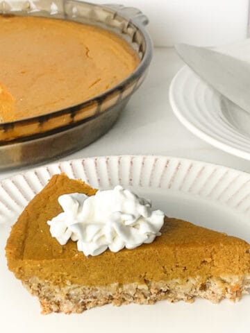 Dairy and gluten-free pumpkin pie slice topped with dairy-free whipped cream on a white plate.