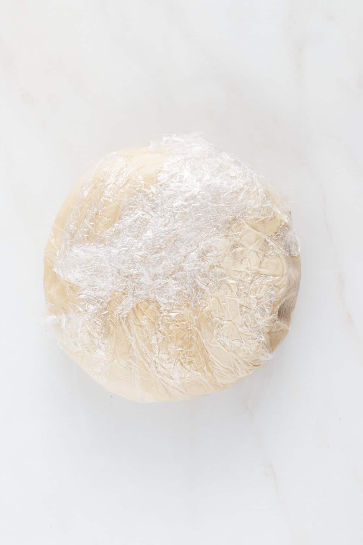 Homemade dairy-free pie crust dough rolled into a disc and covered in plastic wrap.