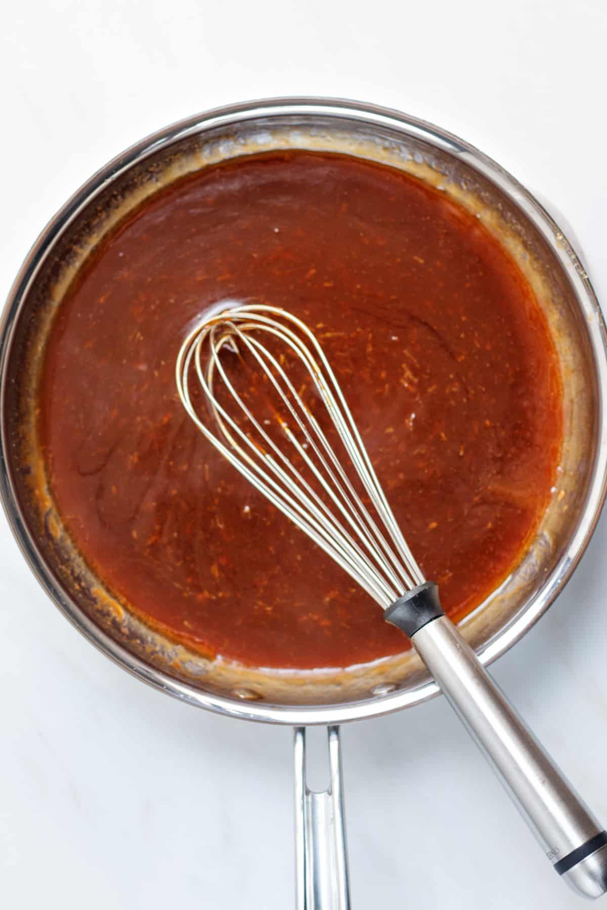 Thickened sesame sauce in a stainless steel pan with a stainless steel whisk in the pan.