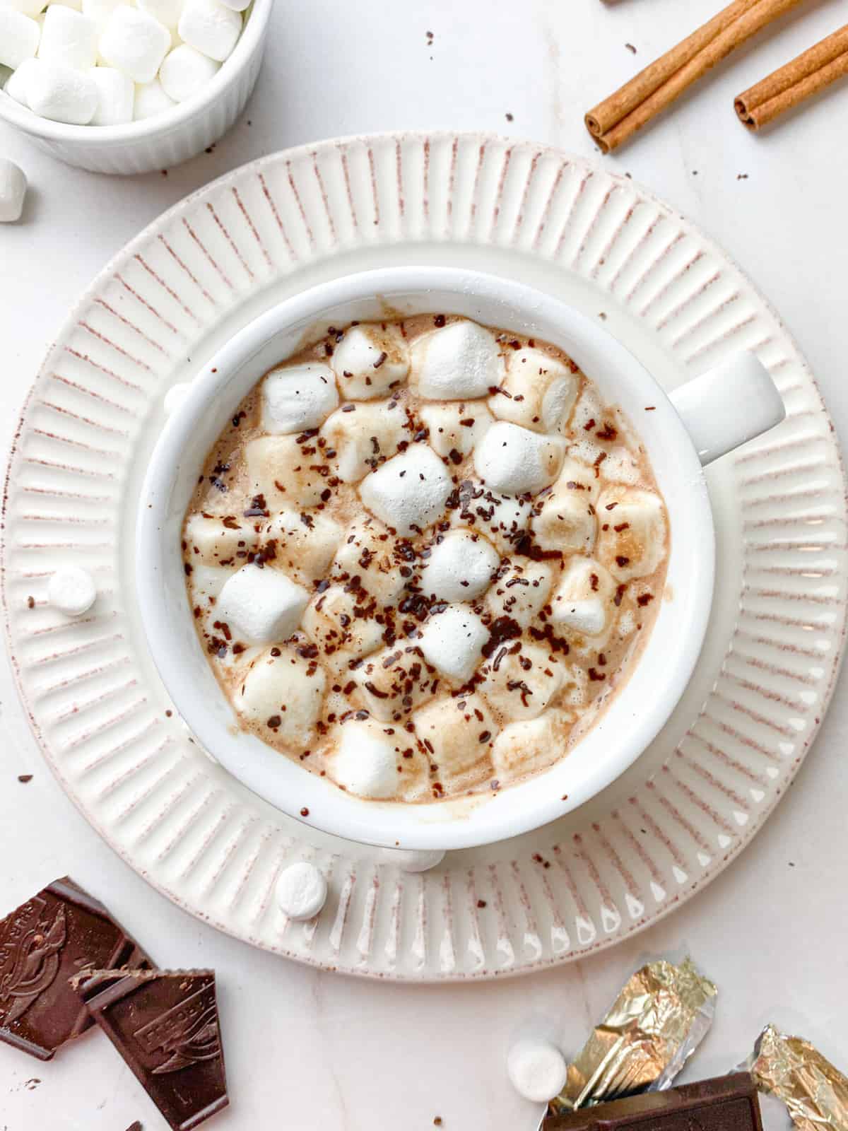 Extra marshmallows in a white mug of vegan hot cocoa with grated melted chocolate on top.