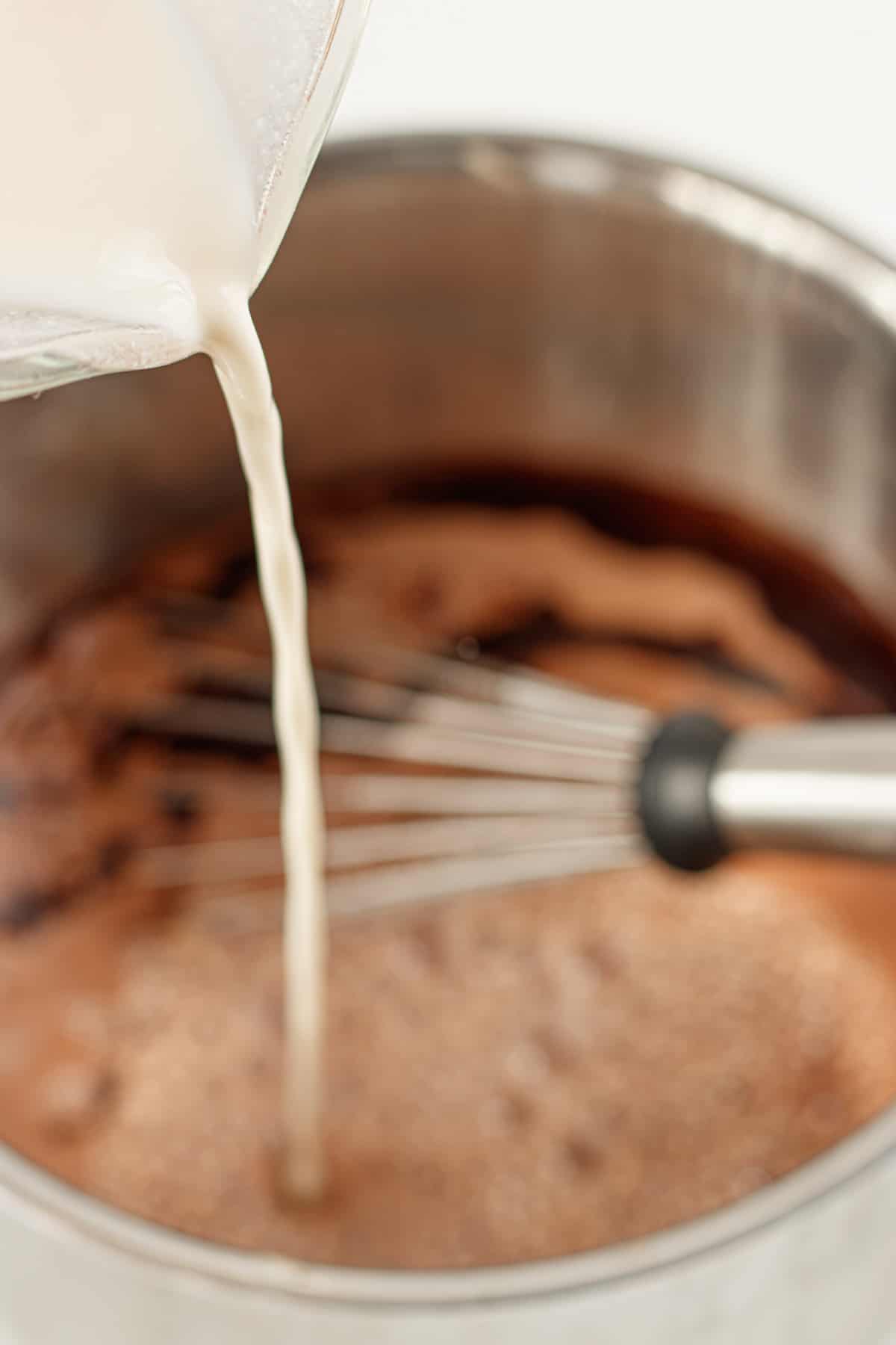 Pouring non-dairy milk into the stainless steel pot of hot cocoa.