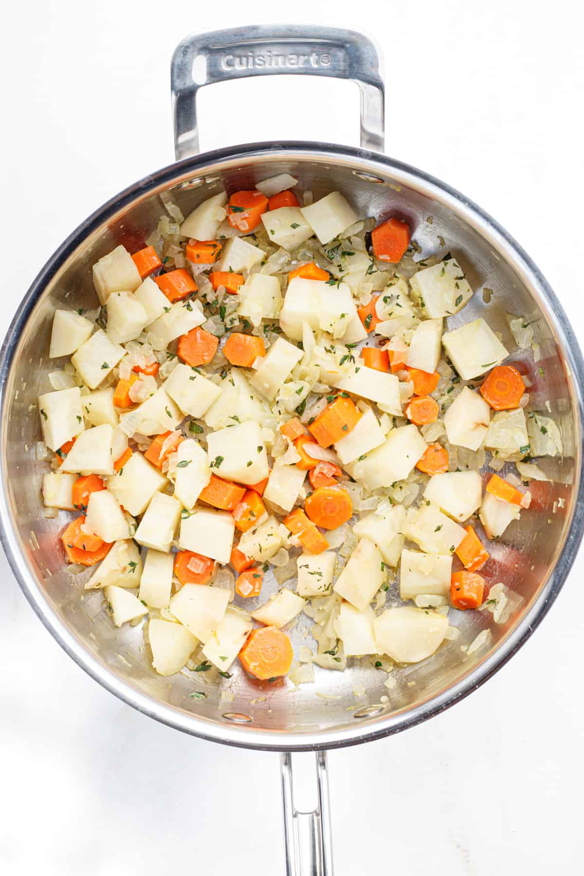 Sautéed onions, carrots, potatoes and herbs in a stainless steel pot.