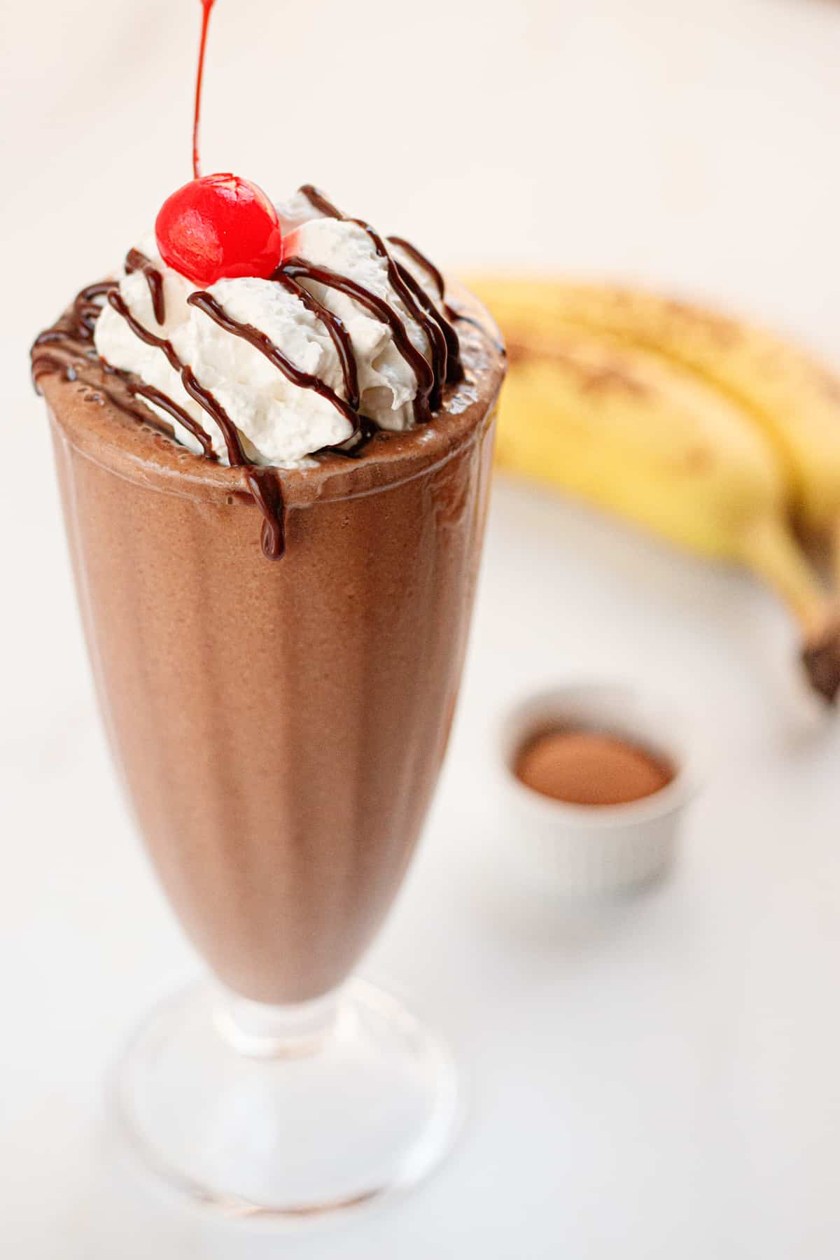 Chocolate banana milkshake with vegan whipped cream and chocolate, topped with a cherry.