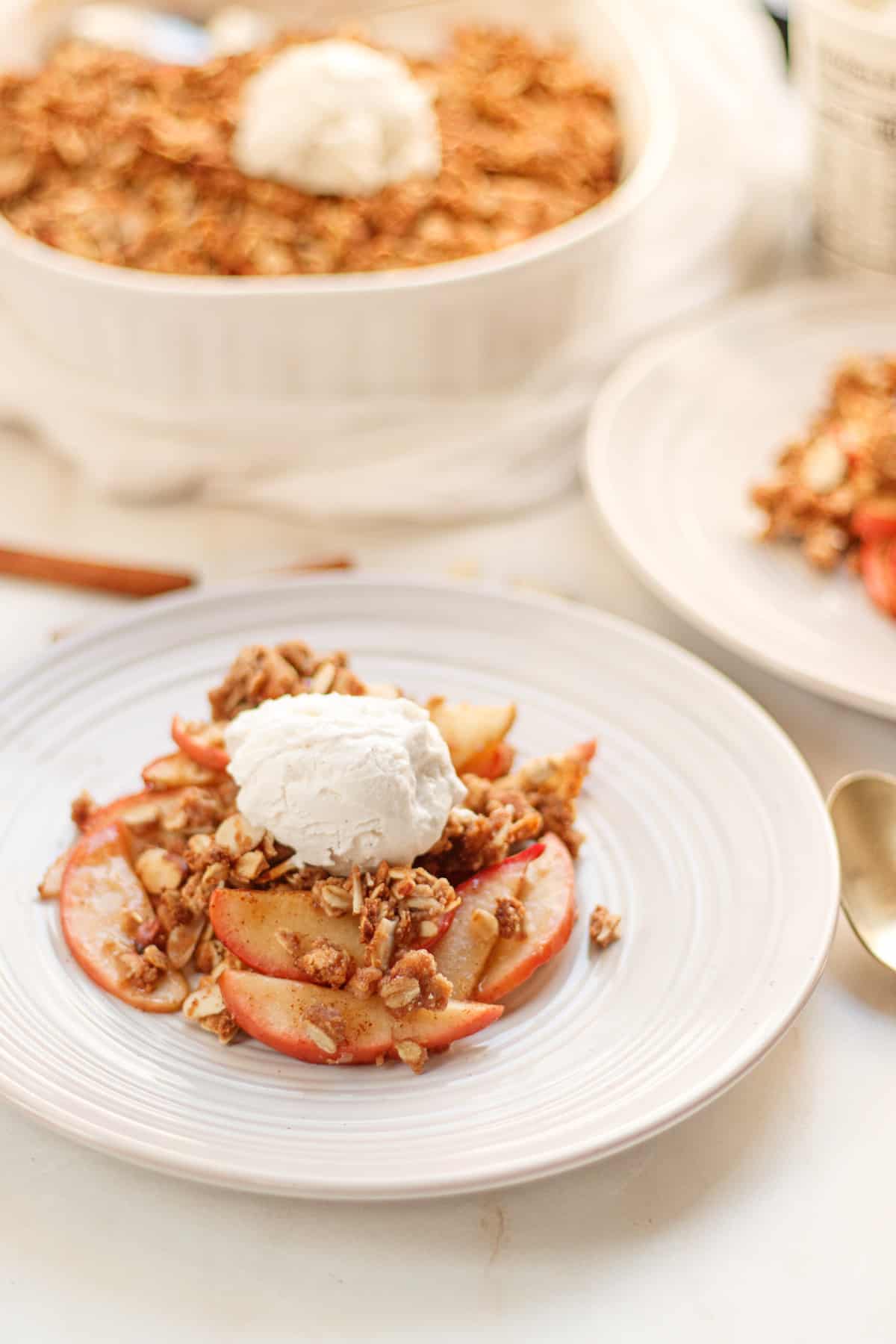 Apple crisp on a white plate, topped with vegan sugar-free ice cream.