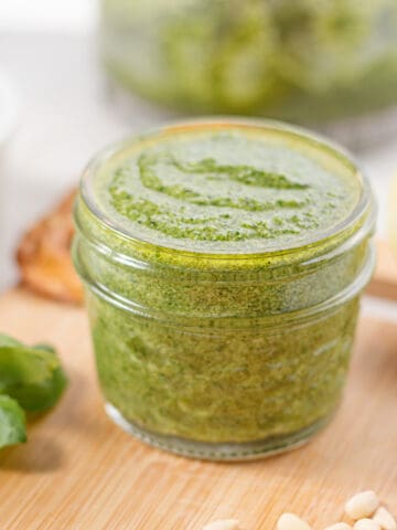 Low-sodium pesto in a glass jar on a wooden cutting board.