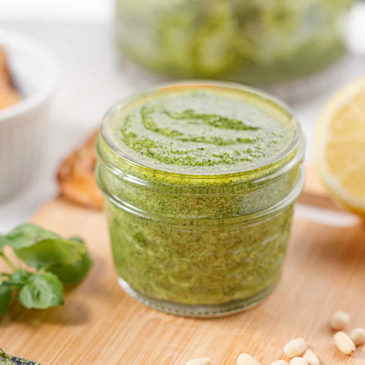 Low-sodium pesto in a glass jar on a wooden cutting board.