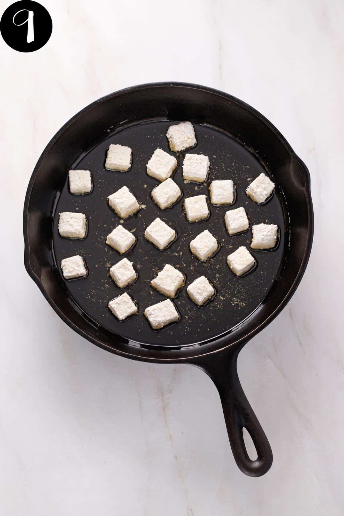 Tofu being shallow fried in a cast iron skillet.