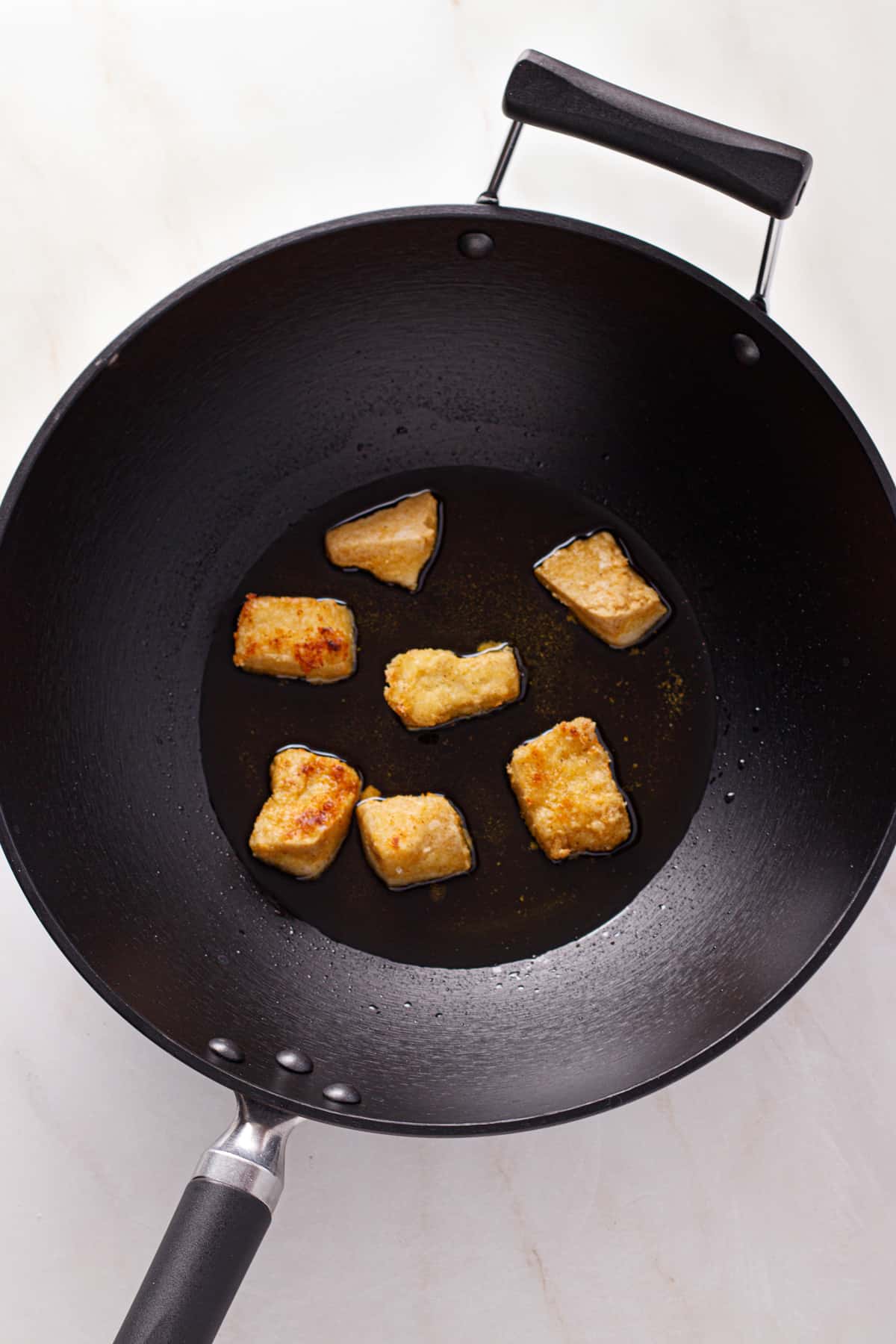 Tofu being shallow fried in olive oil.