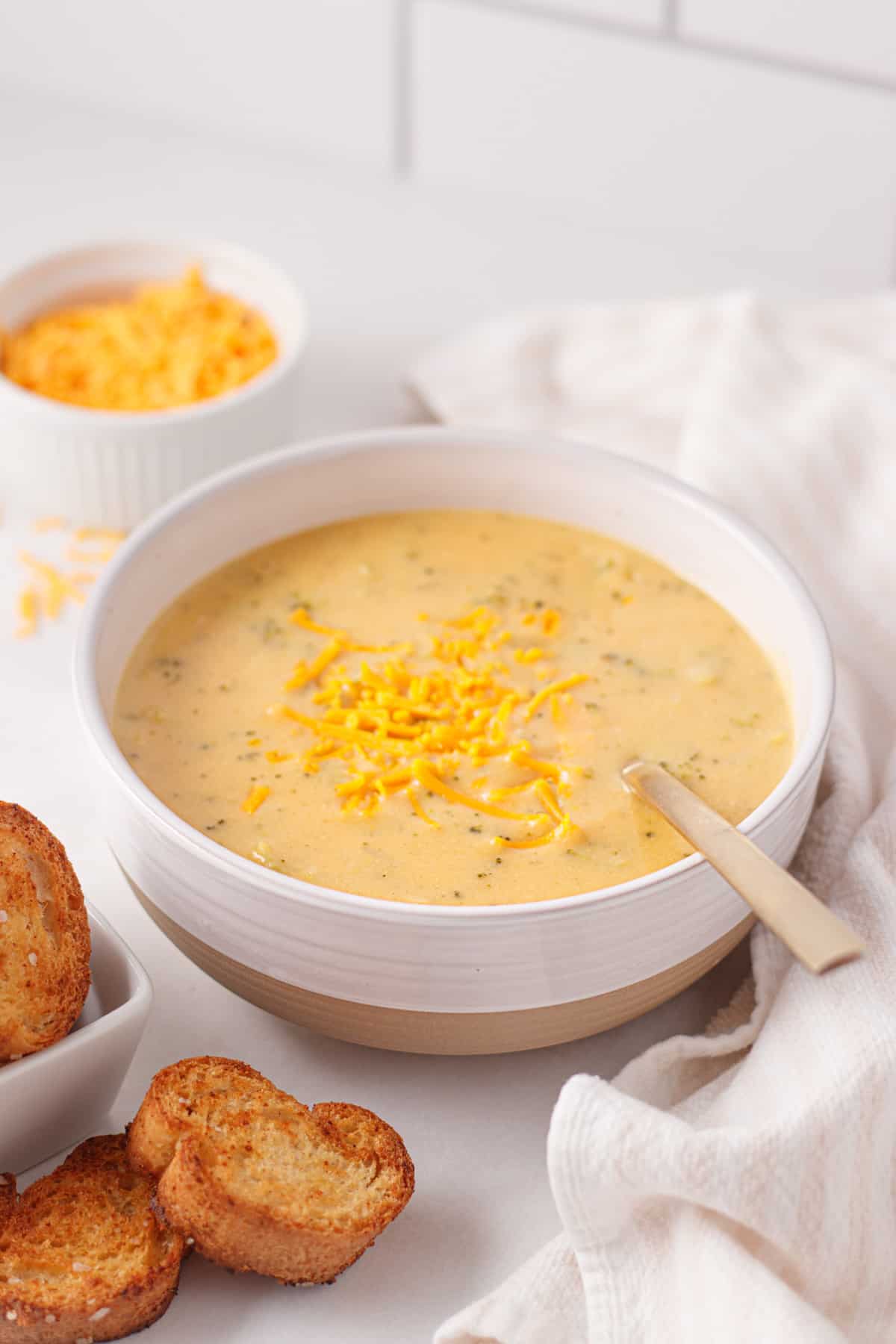 Dairy-free broccoli cheese soup in a white bowl topped with vegan cheese.