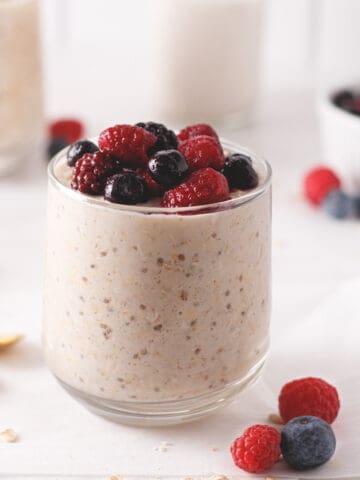 Overnight oats in a glass cup topped with frozen fruit.