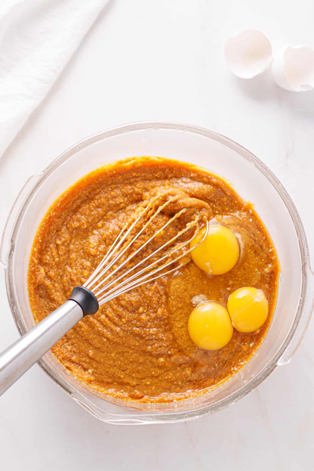 Pumpkin pie filling in a bowl with cracked eggs on top.