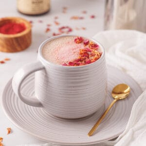 Rose latte in a white mug with dried rose petals on top.