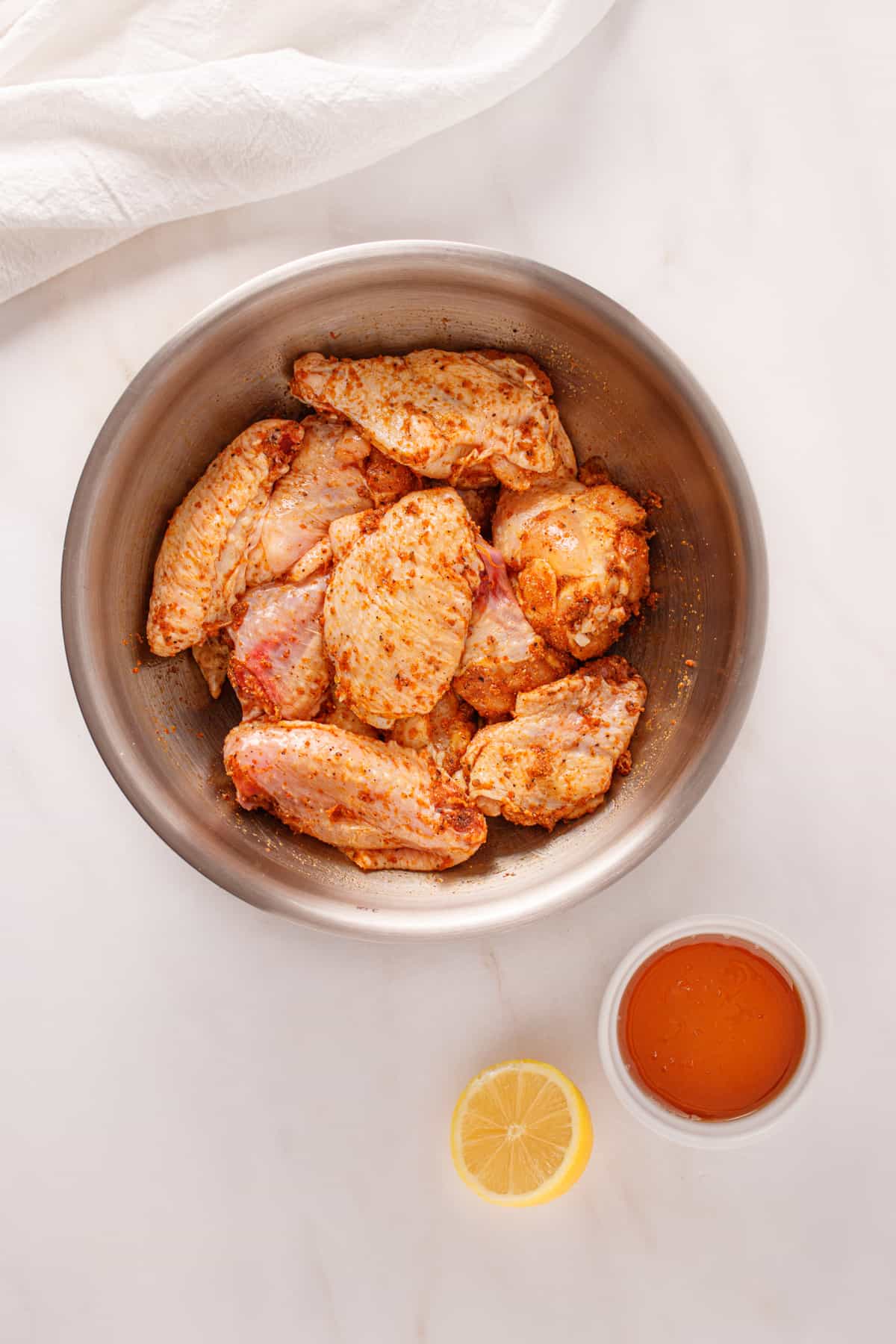 Raw chicken wing pieces in a bowl mixed with spices.