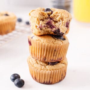 Three dairy-free blueberry muffins stacked with a bite removed.