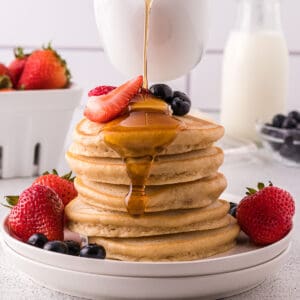 Maple syrup being poured over a stack of pancakes.