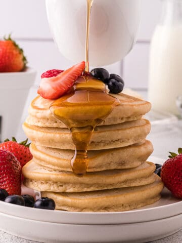 Maple syrup being poured over a stack of pancakes.