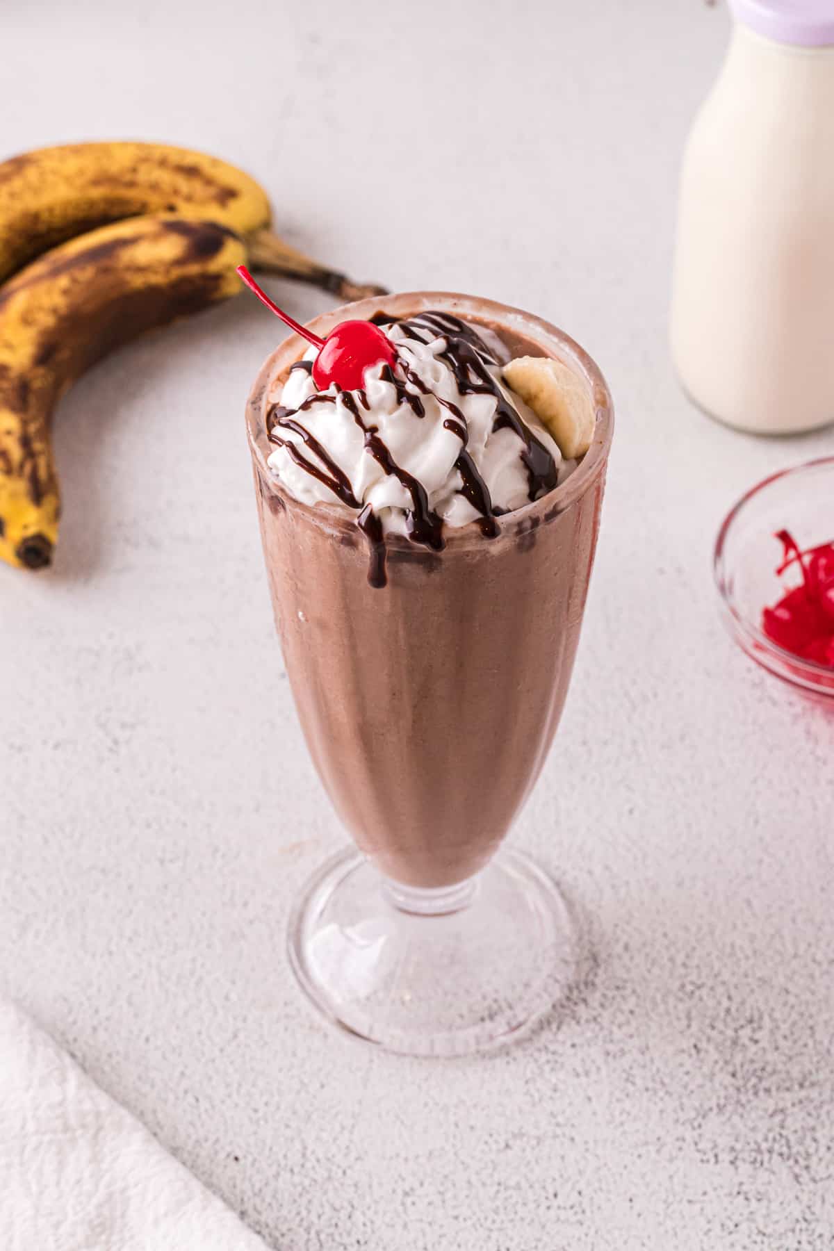 Chocolate banana milkshake with whipped cream, chocolate sauce, a cherry and banana slice.