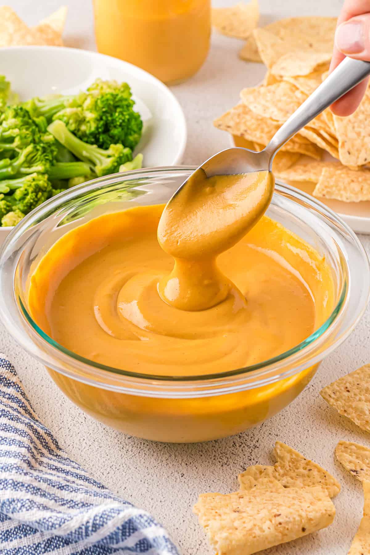 A bowl of vegan cheese sauce with cheese dripping from the spoon.