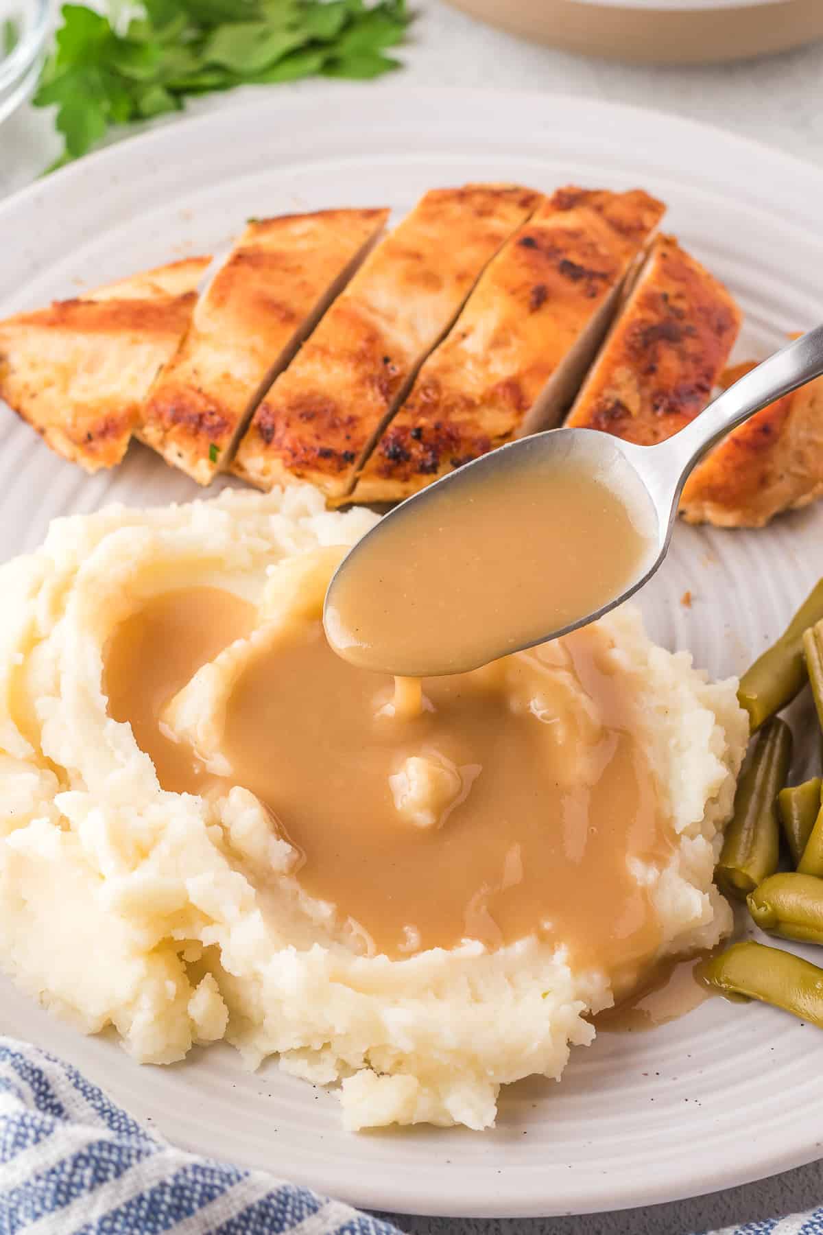 A spoon with gravy dripping on to mashed potatoes.