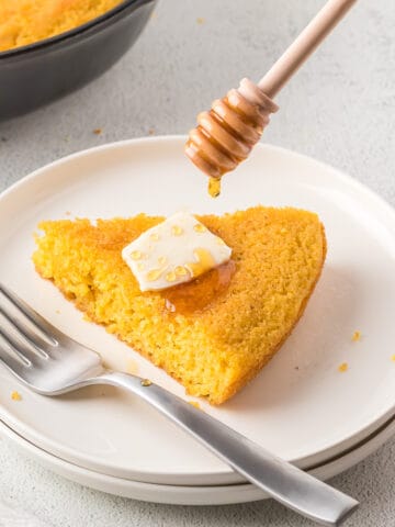 A slice of dairy-free cornbread with non-dairy butter and honey.