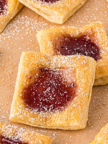 Puff pastry jam tarts on parchment paper with powdered sugar.