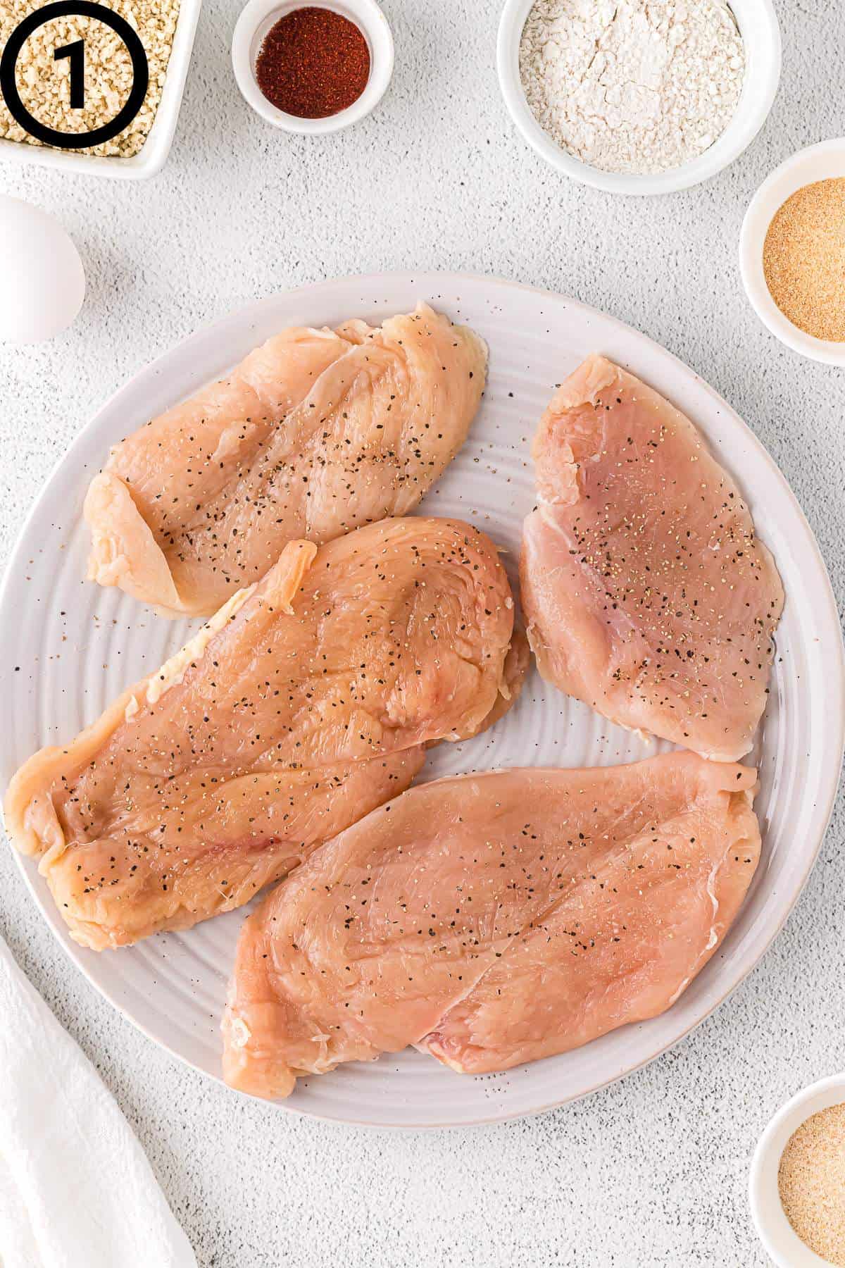 Raw chicken breasts with salt and pepper on a plate.