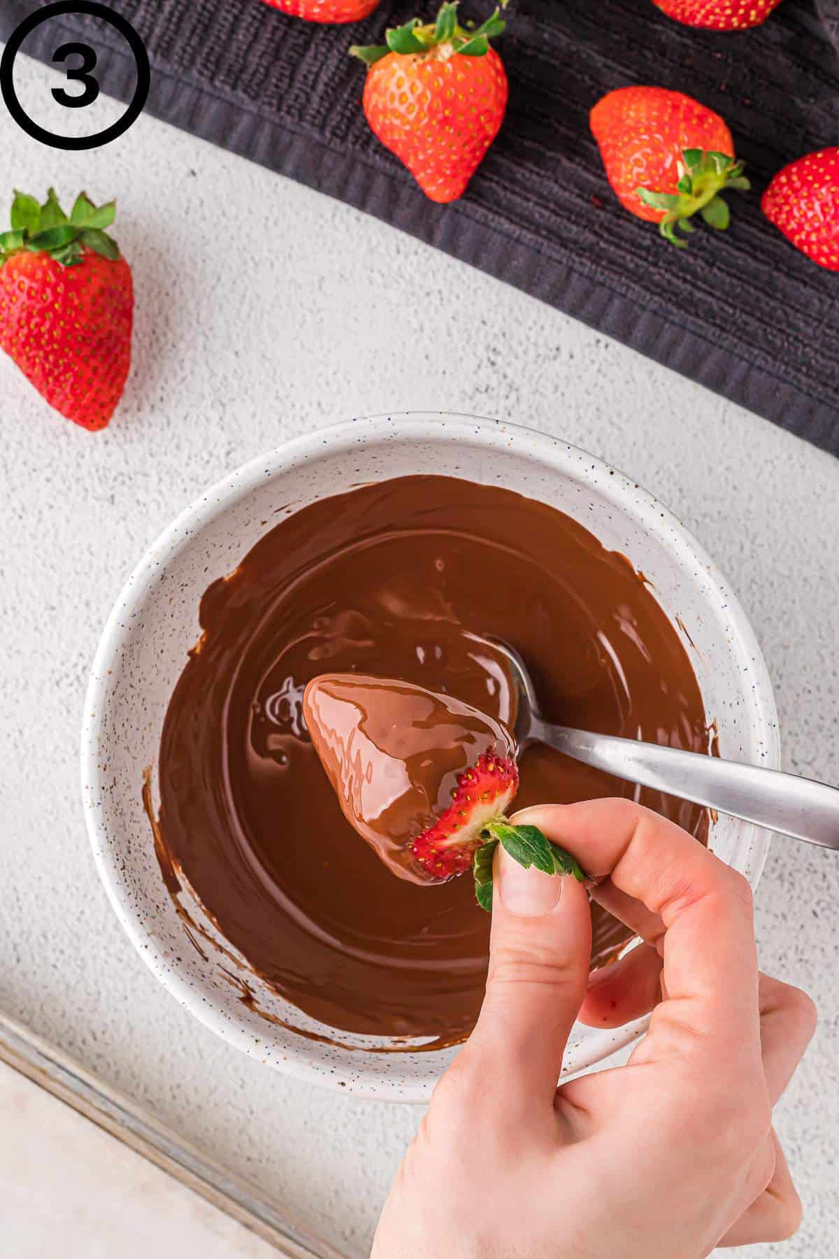Dipping a strawberry into melted vegan chocolate.