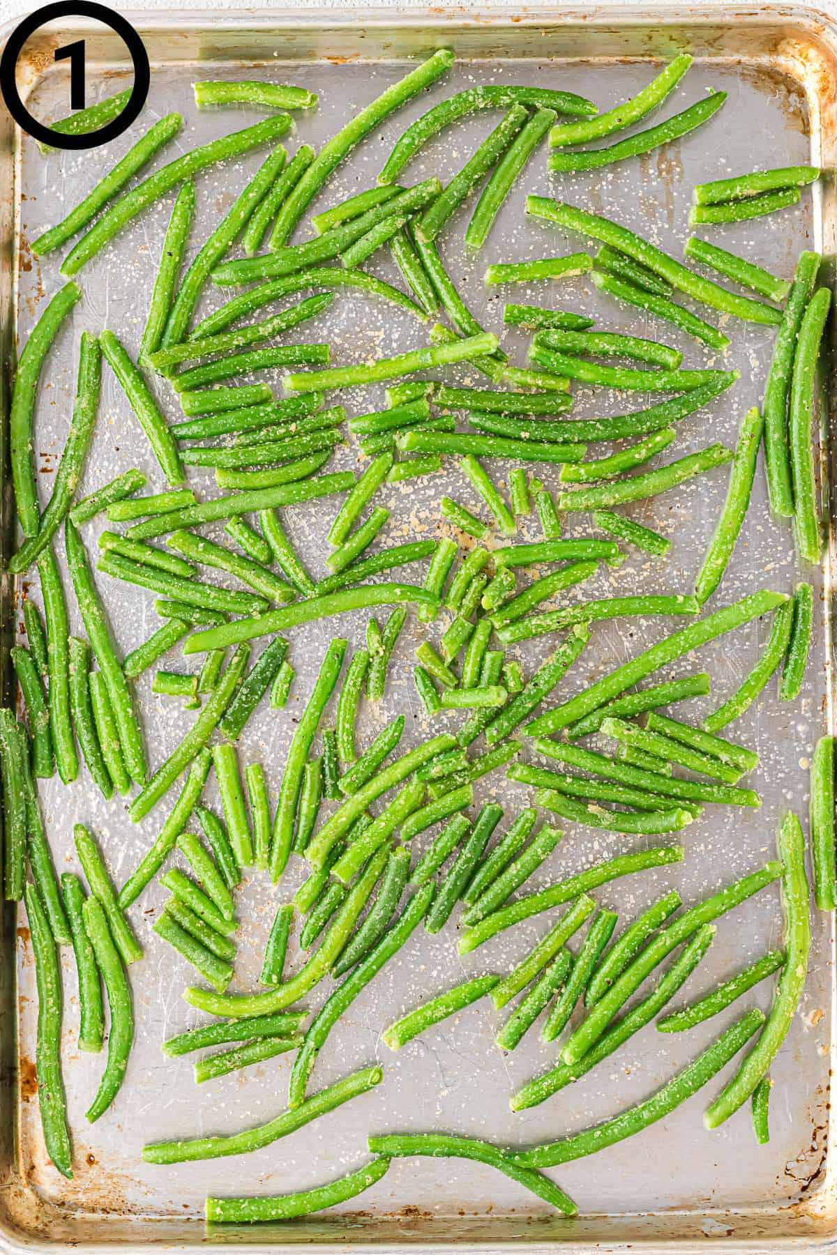 Frozen and seasoned green beans on a greased baking sheet.