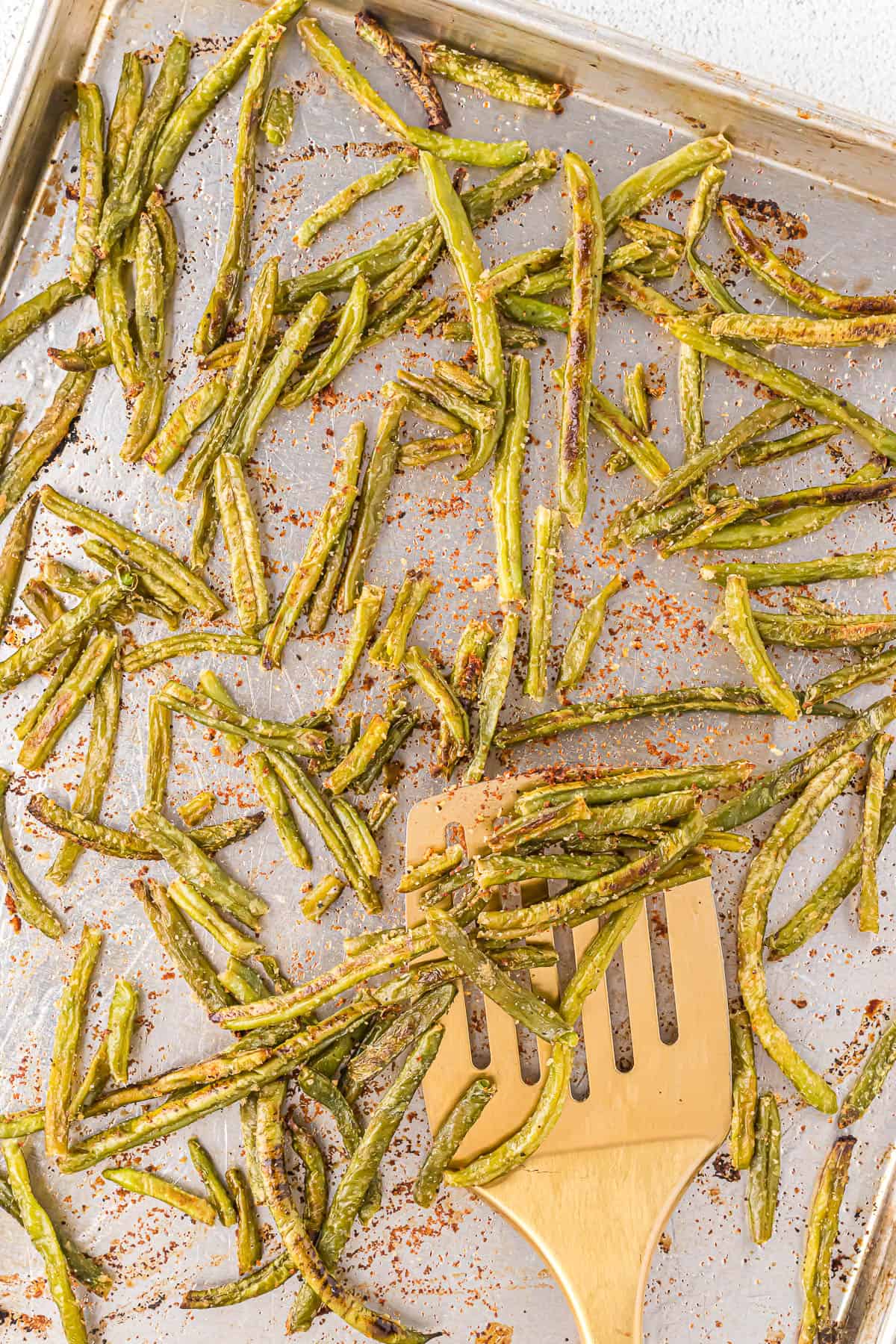 Roasted green beans on a baking sheet with a gold turner.